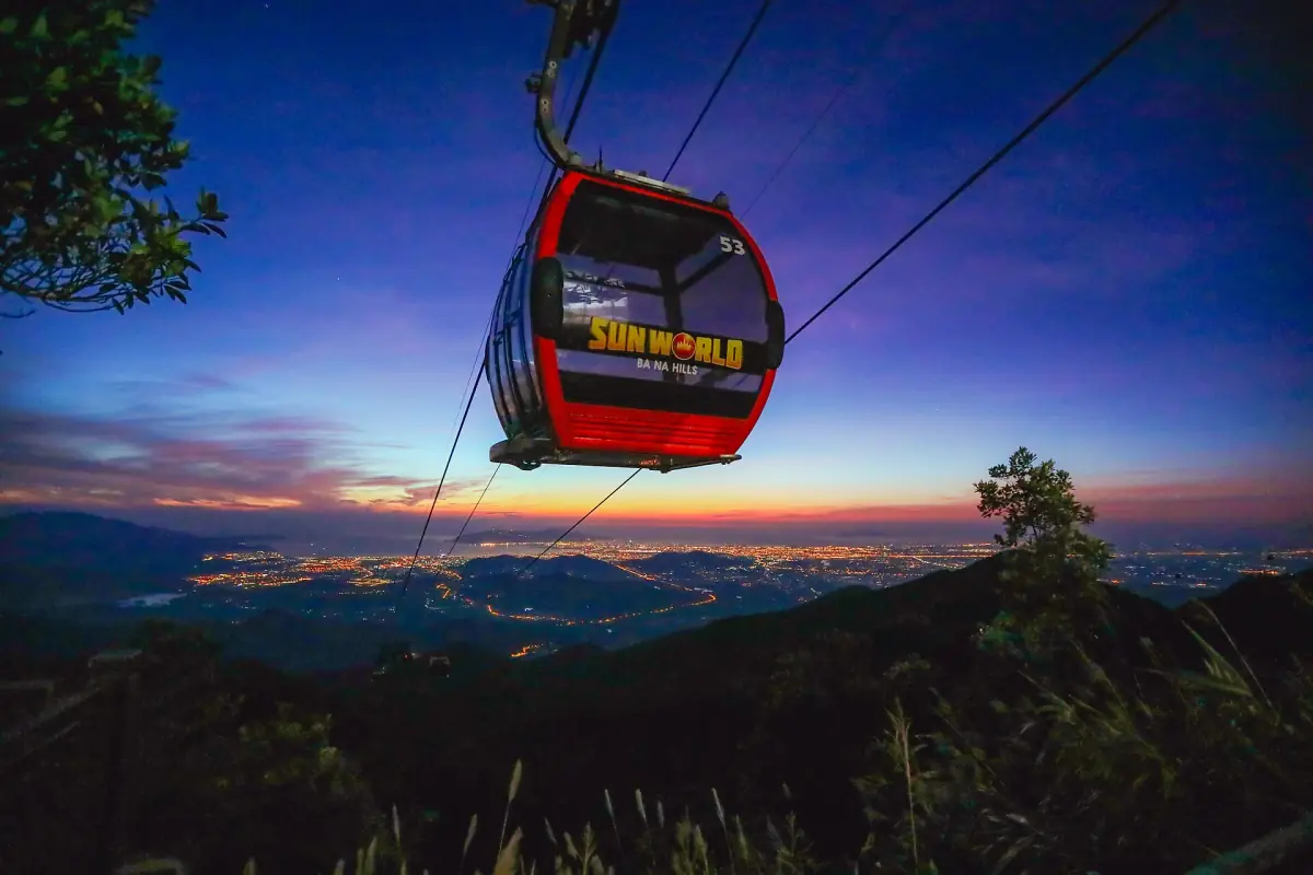 Red cable car cabin above the valley at dusk with city lights below