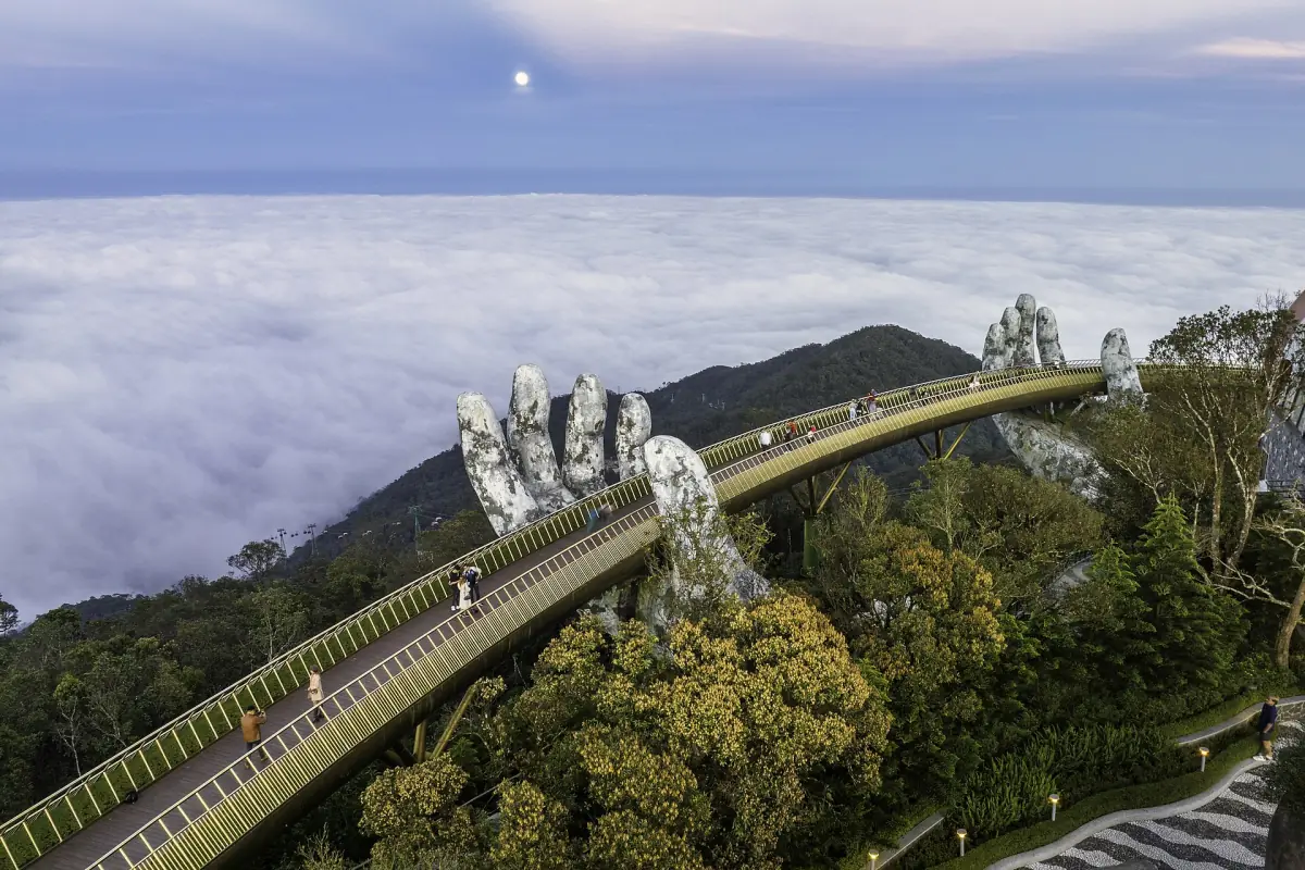 Golden footbridge and stone hands rising above a sea of clouds