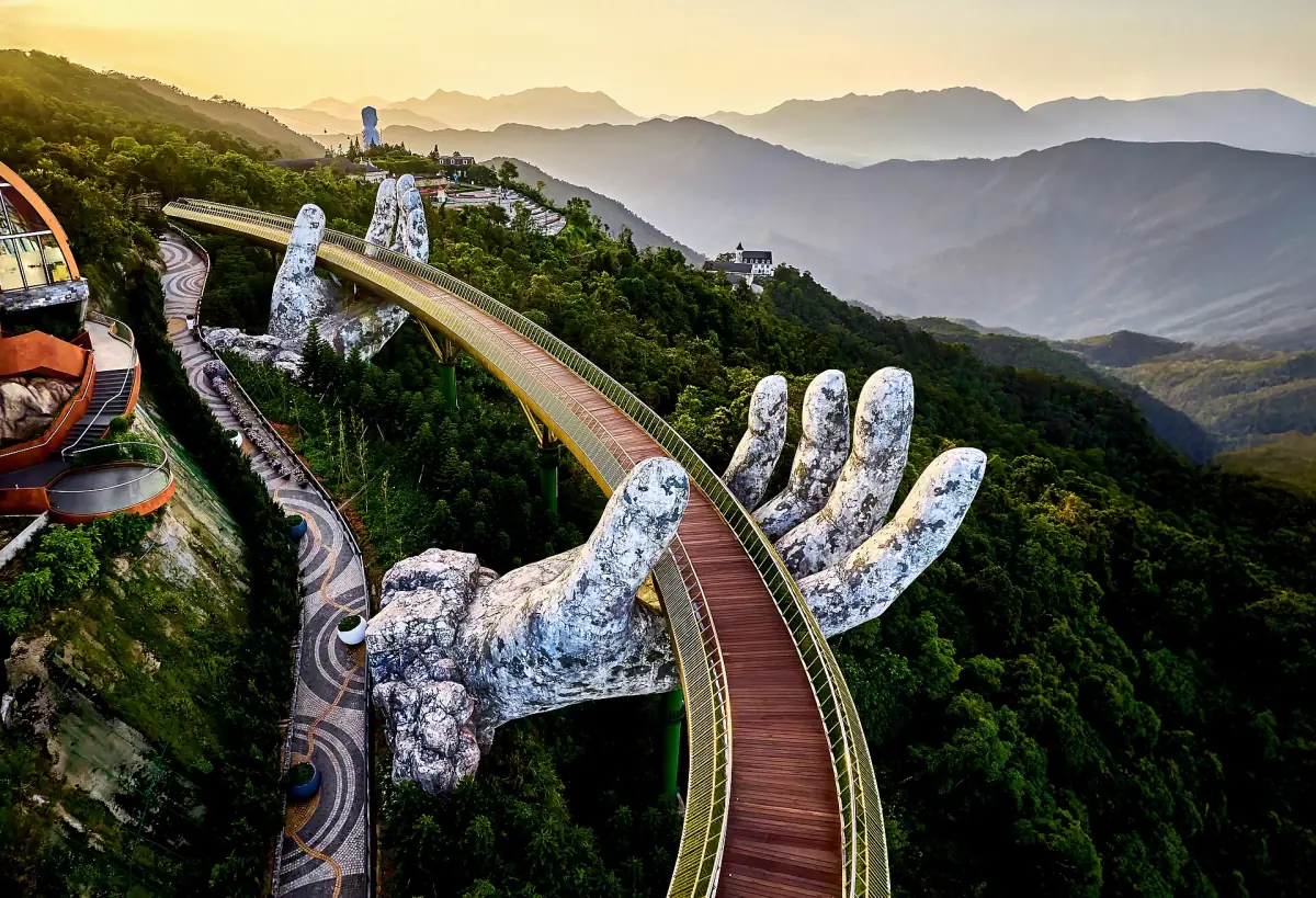 Aerial view of the golden bridge curving along a forested mountain slope