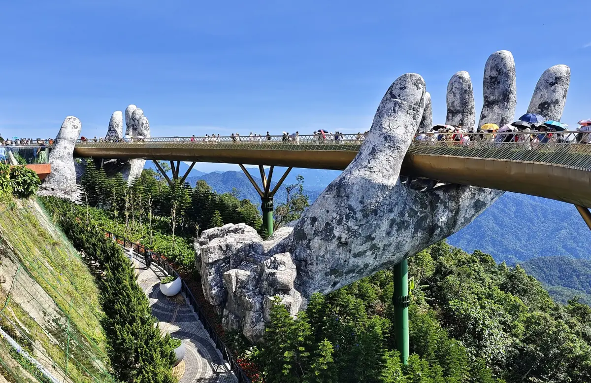 Giant stone hands holding the golden footbridge on a mountain ridge in sunshine