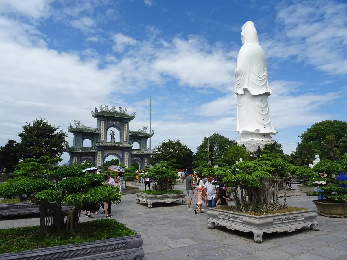 高大的白色觀音像矗立在寺廟大門後方,旁邊有盆栽樹