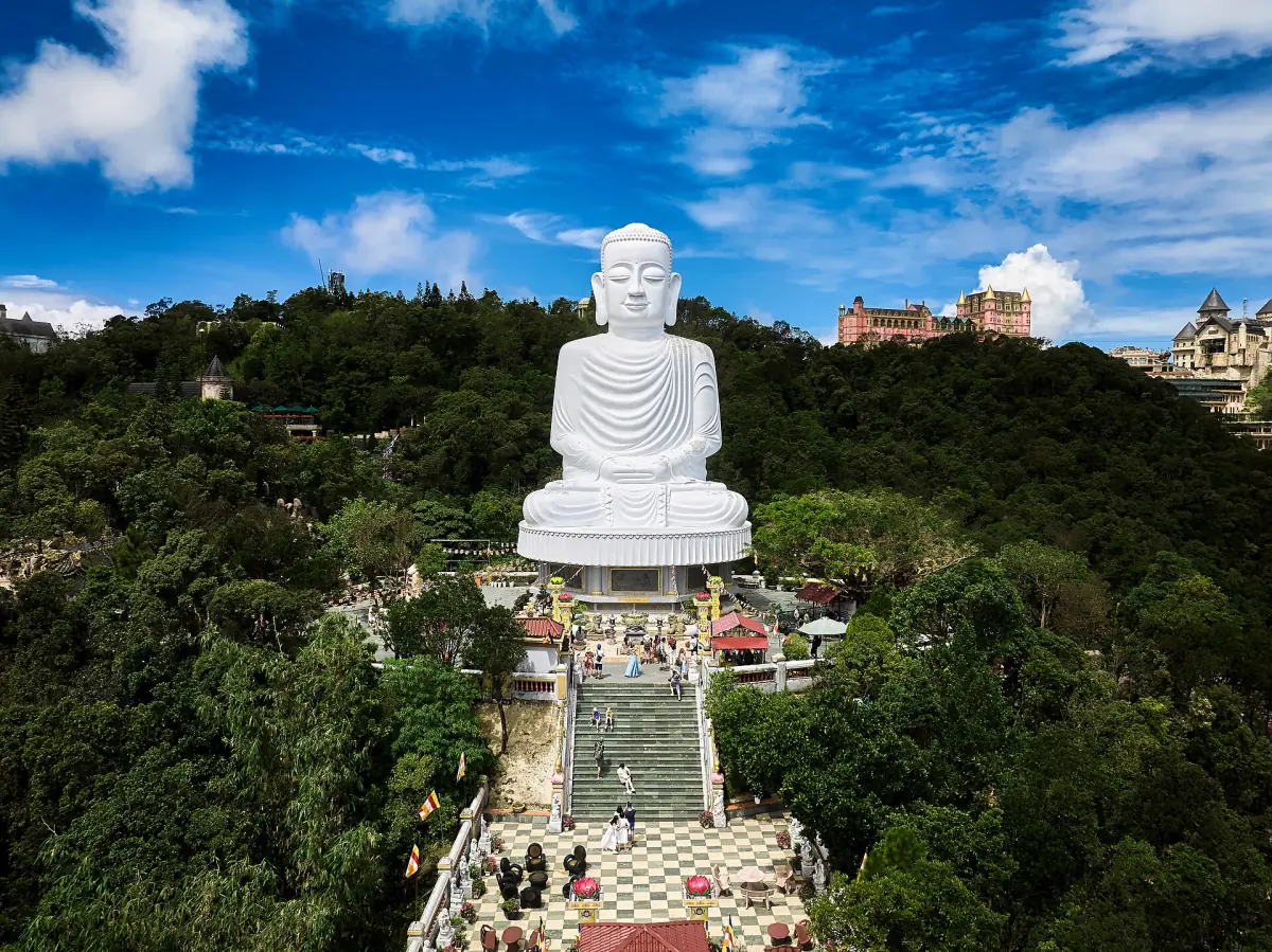 Large white seated Buddha statue above steps in a green mountain setting
