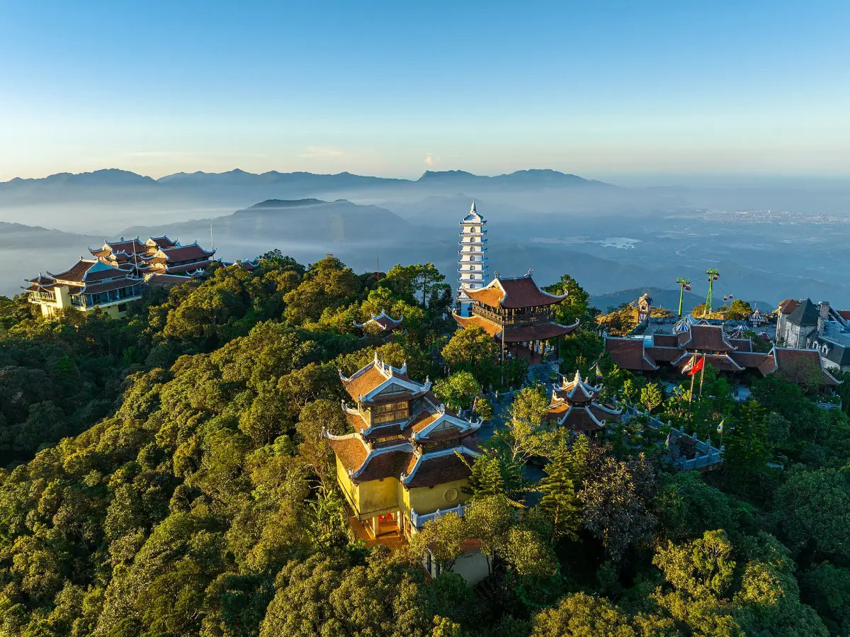 Pagoda towers and temple roofs among trees with mountains in morning haze